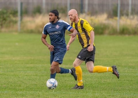 Two soccer players competing for the ball during a match, one in dark blue jersey and one in yellow and black striped jersey