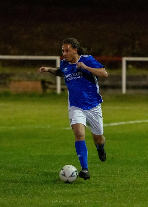 Soccer player in blue and white uniform dribbling ball during night match on grass field