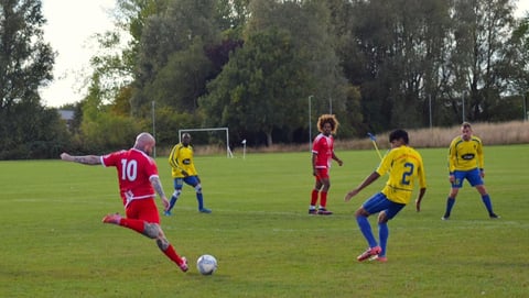 Young soccer players in red and yellow uniforms playing a match on a grass field with trees in the background