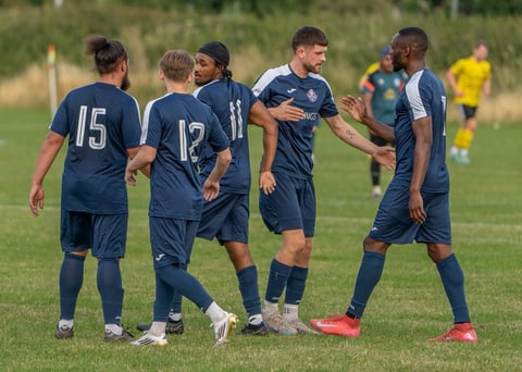 Young soccer players in navy uniforms gathered on a grass field during a youth sports match or practice