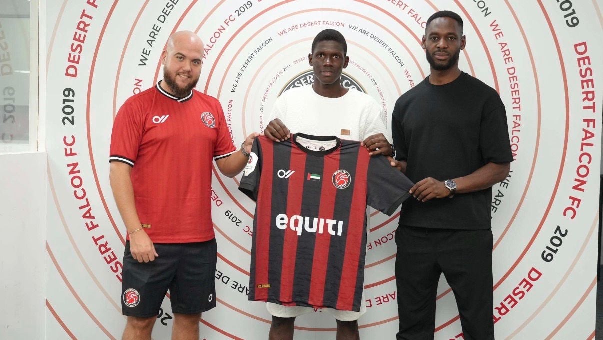 Three men holding a red and black striped football jersey in front of a circular branded backdrop